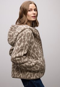 Braune Fleece-Jacke mit Tiermuster, ausgestattet mit Kapuze, Reißverschluss und Seitentaschen. Weiche Textur und kürzer geschnittenes Design.