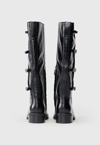 Bottes noires en cuir, arrivant jusqu'aux genoux, avec une texture lisse, ornées de détails en métal argenté et d'une fermeture éclair centrale à l'arrière.