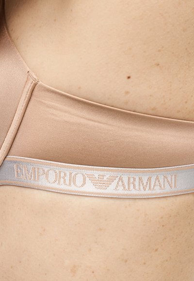 Beige Emporio Armani BH-bånd på hud, med merkevarenavn og logo i lyserosa på elastisk stripe.