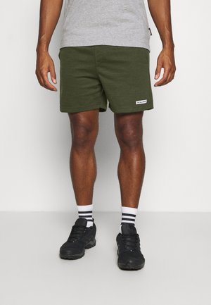 Mann trägt olivgrüne Shorts mit einem kleinen weißen Jack & Jones-Label, graues Hemd, schwarze Turnschuhe und weiße Socken mit schwarzen Streifen.