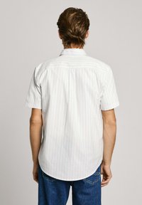 Camisa blanca de manga corta con rayas verticales azul claro, dobladillo curvo y cuello estándar. La tela parece suave y ligera.