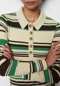 Sweter w paski z prążkowanego materiału na beżowym tle, z zielonymi, brązowymi, różowymi i kremowymi paskami. Posiada kołnierzyk oraz sześć dekoracyjnych guzików.