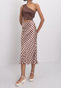 Ruskea yksivärinen olkaimeton paita yhdistetty ruskeaan ja valkoiseen ruudulliseen midihameeseen; sileä satiinipinta, viimeistelty vaaleansävyisillä korokepohjaisilla sandaaleilla.