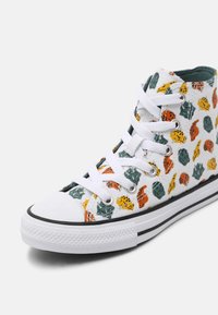 Basket montante en toile avec lacets et semelle blancs, décorée de motifs de feuilles multicolores orange, jaune et vert.