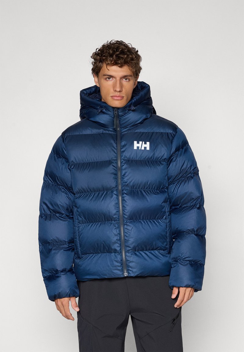 Veste matelassée bleu marine avec des sections quiltées horizontales, un col haut et une fermeture éclair à l'avant. Comprend un logo sur la poitrine gauche.