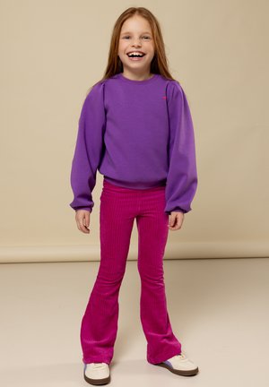 Paarse sweatshirt met geplooide mouwen en een klein geborduurd hartje, gecombineerd met roze corduroy flared broek met verticale strepen.