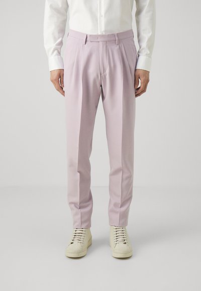 Helle rosa maßgeschneiderte Hose mit Falten, aus glattem Stoff. Kombiniert mit weißen Sneakern, die ein minimalistisches Design und Schnürsenkel aufweisen.