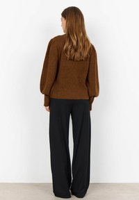 Bruine geribde trui met opgeblazen mouwen, gecombineerd met losse zwarte broek. De textuur is zacht, met een getailleerd lijfje en een ontspannen pasvorm.