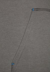 Tissu gris à la texture douce. Comprend une poche avec des coutures bleues et des coutures soignées. La surface présente un motif subtil, ajoutant un intérêt visuel.