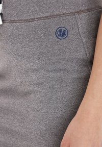 Sive prilegajoče trenerke iz mehkega materiala, ki imajo teksturirano površino, elastičen pas in majhen mornarsko moder logotip na strani.