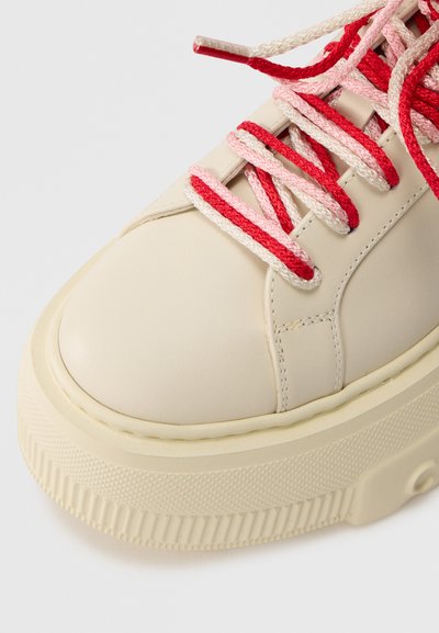 Αθλητικό παπούτσι από δέρμα εκρού με στρογγυλεμένη μύτη, χοντρή λαστιχένια σόλα και κορδόνια σε αντίθετα κόκκινα και ροζ χρώματα. Υφή στη σόλα για καλύτερη πρόσφυση.