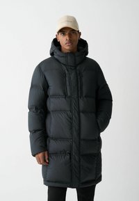 Črno puffer jakno s kapuco, ki ima prešit dizajn, dva sprednja žepi z zadrgo in sprednjo zadrgo za zapiranje. Gladka, sijoča tekstura.