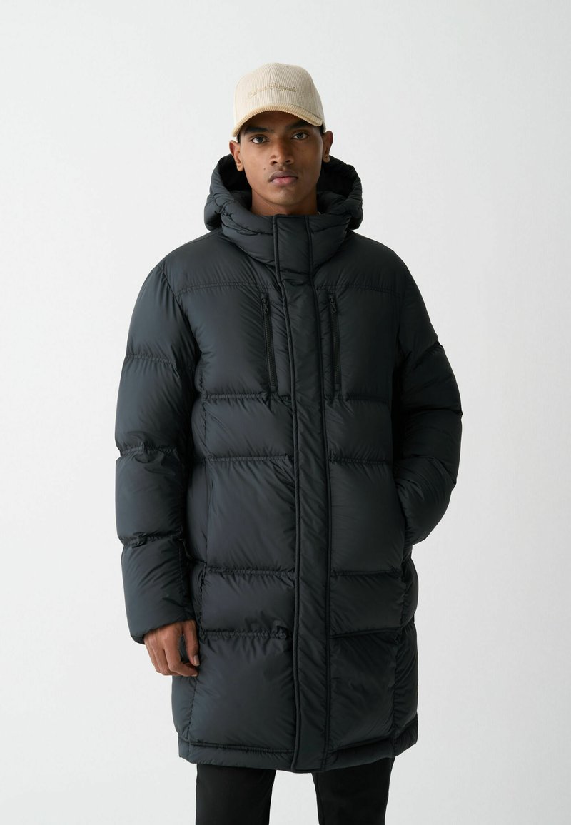 Črno puffer jakno s kapuco, ki ima prešit dizajn, dva sprednja žepi z zadrgo in sprednjo zadrgo za zapiranje. Gladka, sijoča tekstura.