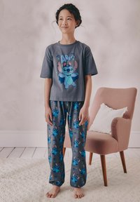 Graues kurzärmeliges Pyjama-Set mit einer Cartoonfigur in Blau- und Rosatönen, kombiniert mit gemusterten Hosen, die die Figur auf einem grauen Hintergrund zeigen.