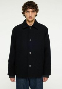 Svart ullblandad kappa med krage, fem knappar, två sidofickor och manschetter. Fin struktur med en skräddarsydd passform.