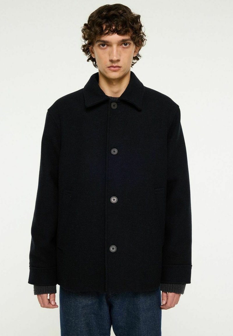 Svart ullblandad kappa med krage, fem knappar, två sidofickor och manschetter. Fin struktur med en skräddarsydd passform.