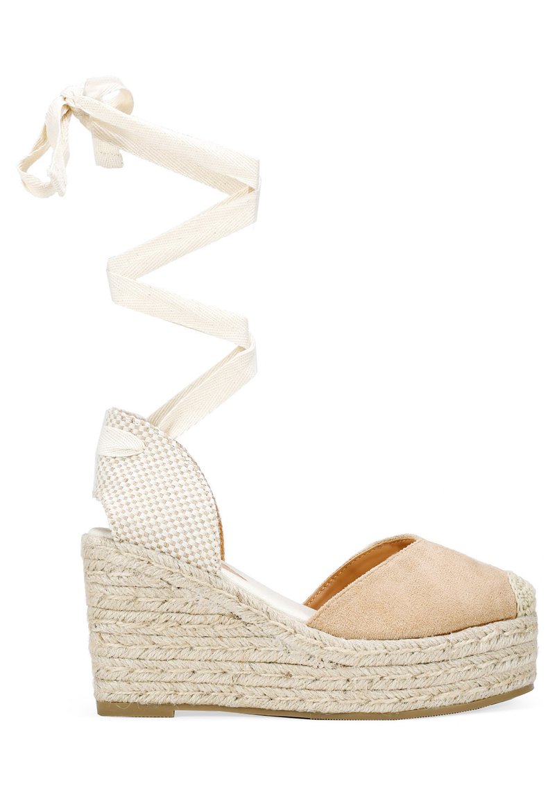 Sandalia de cuña con parte superior de ante beige, suela de yute trenzado y cordones de tela blanca en espiral subiendo por el tobillo. Diseño de punta abierta con un acento texturizado.