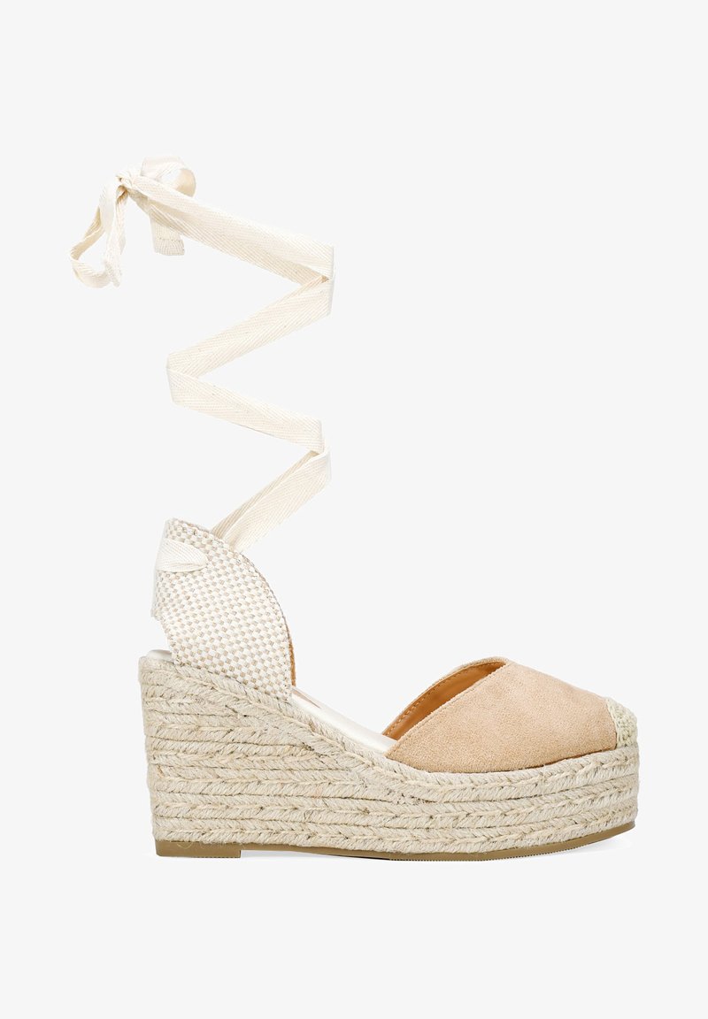 Sandale compensée avec une tige en daim beige, semelle en jute tressé et lacets en tissu blanc s'enroulant autour de la cheville. Design à bout ouvert avec une accent texturé.