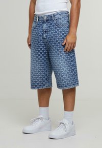 Pantalones cortos de mezclilla azul con un patrón geométrico, de longitud a mitad del muslo, cinco bolsillos y dobladillo deshilachado, combinados con zapatillas blancas y calcetines cortos.