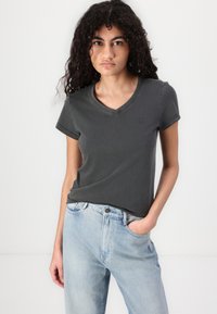 Tricou V cu decolteu în nuanță gri închis, confecționat din bumbac, cu mâneci scurte și un logo subtil. Asortat cu blugi din denim de culoare albastru deschis.