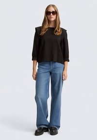 Zwarte cropped top met pofmouwen, gecombineerd met lichtblauwe wijde jeans en zwarte platform schoenen. Model draagt een donker zonnebril.