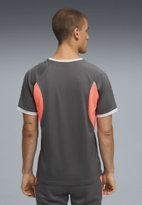Camiseta atlética gris de mangas cortas, con paneles laterales en coral brillante y cuello blanco. Material ligero y transpirable.
