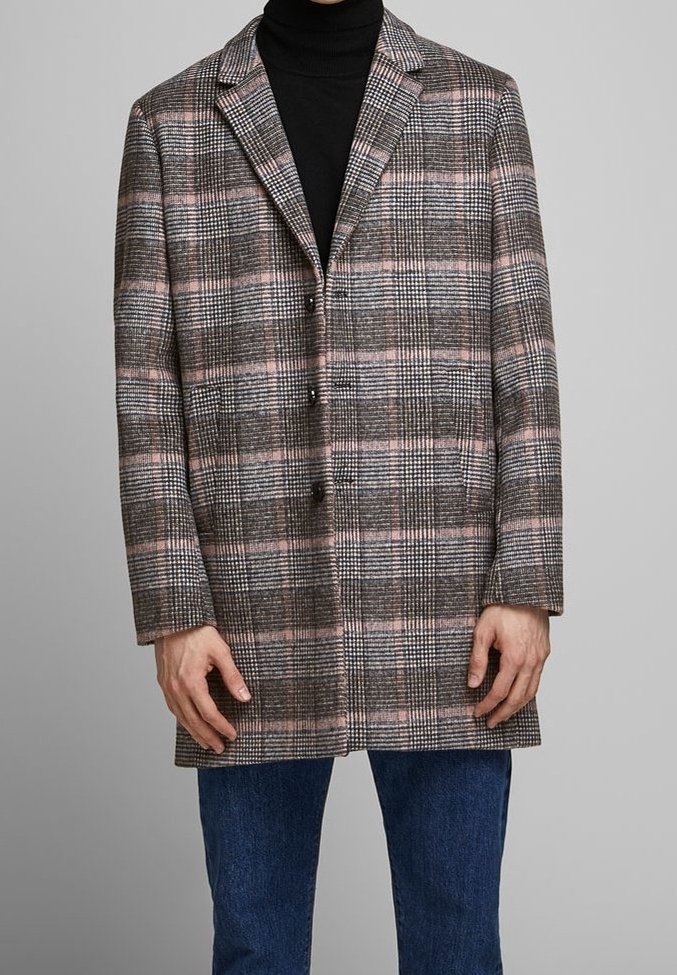 Cappotto a quadri marrone con accenti rosa, dotato di colletto a rever, chiusura con tre bottoni e taglio di lunghezza media. Indossato sopra un dolcevita nero.