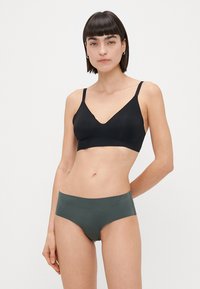 Svart trådlös bralette med v-ringad design som matchas med mörkgröna mid-rise trosor. Båda har en slät, sömlös yta.