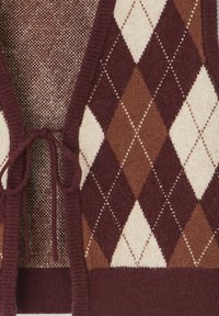 Cardigan à motif argyle marron et crème avec une fermeture à nouer, présentant une texture douce et un design tricoté, mettant en avant des couleurs contrastantes.