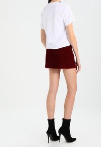 Vitt bomulls-t-shirt matchad med en röd kordfloret mini kjol, med en texturerad yta och fransad kant, kompletterad med svarta ankelskor.