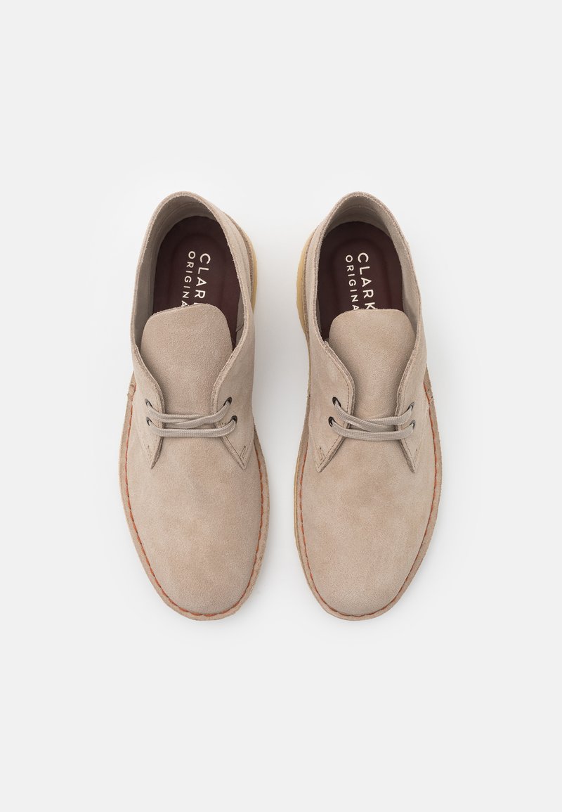 Beige Wildlederschuhe mit einer abgerundeten Zehenpartie, leichtem Aufbau, dünnen Schnürsenkeln und einer kontrastierenden hellbraunen Sohle.