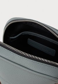 Világosszürke bőr táska texturált felülettel, ezüst cipzárral és fekete belső térrel, amelyben egy további zseb és márkajelzés található.