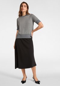 Top in maglia grigia a maniche corte con bordo a coste più scuro, abbinato a una gonna maxi nera fluente e sandali con tacco a punta nera con dettaglio a fiocco.