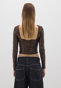 Top corto a maniche lunghe nero con paillettes, caratterizzato da una ampia schiena quadrata, abbinato a jeans skinny neri a vita alta con tasche posteriori doppie.