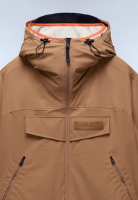 Giacca impermeabile marrone con cappuccio, dotata di zip frontale, tasca sul petto e dettagli neri. Fodera interna arancione e cordini regolabili.