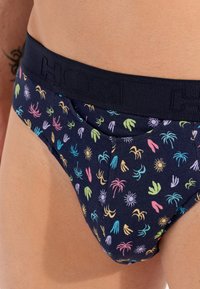 Marineblaue Unterhose mit bunten, kleinen tropischen Mustern. Verfügt über einen breiten, strukturierten schwarzen Gummibund mit dem Markennamen. Weiches Material.