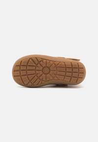 UGG tøffelsåle, gummi i en tan farge, med strukturert mønster for grep og stabilitet. Rund tådesign.