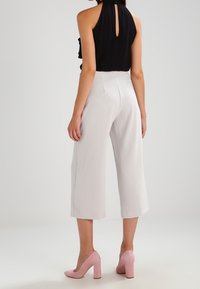 Helle graue Culottes mit einer hohen Taille, kombiniert mit einem schwarzen ärmellosen Oberteil mit einem Rückenausschnitt. Getragen mit rosa Absatzschuhen.