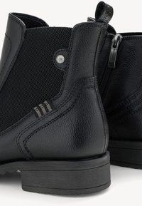Paire de bottines noires en cuir avec côtés texturés, fermeture éclair, détails de couture et petite languette à l'arrière.