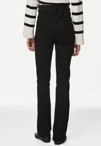 Jeans acampanados de mezclilla negra de talle alto con un acabado texturizado, que cuentan con dos bolsillos traseros y costuras resistentes. Un calzado negro completa el conjunto.