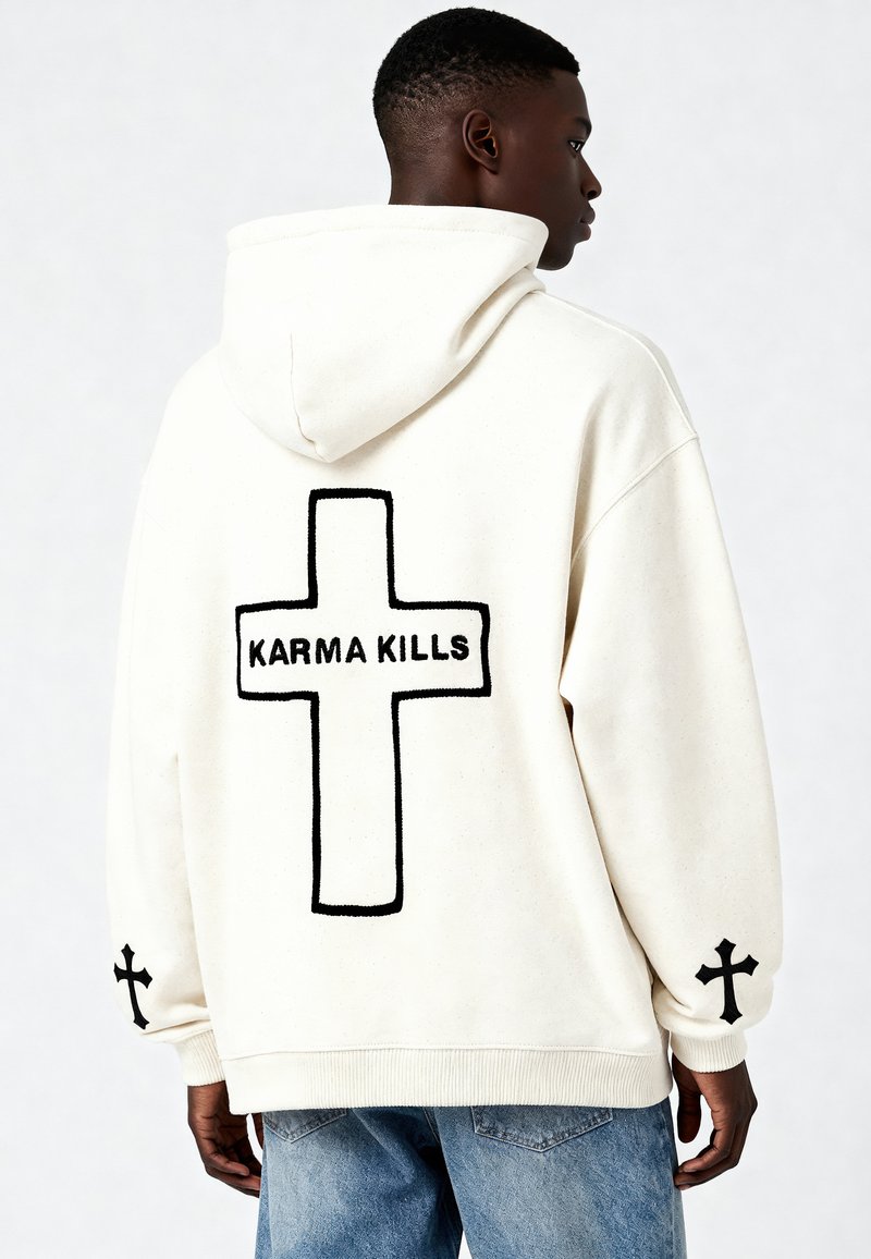 Felpa con cappuccio crema, caratterizzata da una grande croce nera e la scritta "KARMA KILLS" sul retro, con croci più piccole su ogni manica.