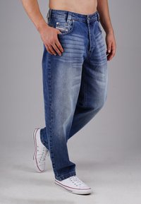 Blue denim jeans with a relaxed fit, featuring faded areas and five pockets. Paired with white sneakers with red accents.