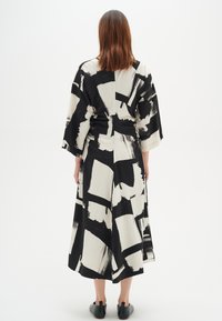 Pitkä musta-valkoinen kuvioitu mekko, jossa on leveät hihat ja A-linjainen siluetti, joka esittelee abstrakteja siveltimen vetoja ja kevyttä kangasta.
