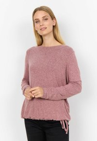 Lichtroze sweater met lange mouwen, voorzien van een gestructureerde afwerking, ronde halslijn en een gather-halslijn met trekkoord. Gepaard met zwarte broek.