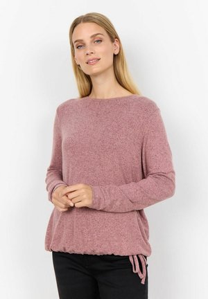 Pull long à manches longues rose clair avec une finition texturée, col rond et ourlet froncé avec lien de serrage. Associé à un pantalon noir.