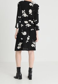Vestido negro con mangas tres cuartos, que presenta patrones florales blancos y un lazo en la cintura. Se lleva con botas cortas negras brillantes.