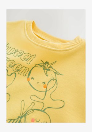 Yellow sweatshirt with ribbed neckline. Features green illustrations and text, depicting smiling fruits with embroidered accents in orange.