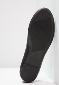 Semelle de chaussure noire avec zones d'adhérence texturées et taille 37 embossée près du talon, photographiée sur un fond blanc.