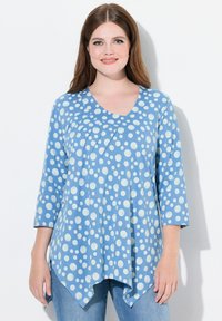 Blauwe tuniek met witte stippen, driekwart mouwen, V-hals en asymmetrische zoom. Gemaakt van een zachte stof met een gestructureerde afwerking.