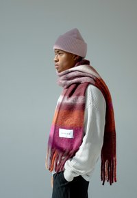 Gebreide wollen sjaal met levendige rode, roze en oranje gradient strepen en franjes aan de randen; bevat een wit label met de tekst "ARCTIC FOX."